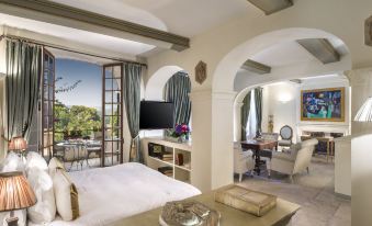 a bedroom with a bed , desk , and television is shown with an arched doorway leading to a balcony at Chateau le Cagnard