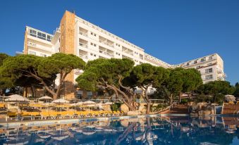 a large hotel building with a swimming pool and trees surrounding it , creating a picturesque scene at Htop Caleta Palace #HtopBliss