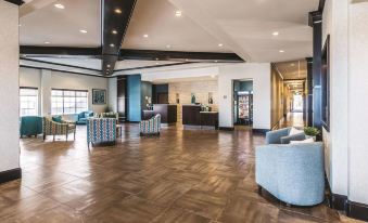 a spacious , well - lit hotel lobby with wooden floors and furniture , including couches and chairs , as well as a reception desk at La Quinta Inn & Suites by Wyndham Dallas Grand Prairie South