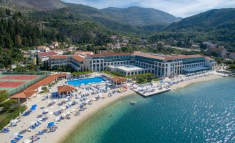 a large , white building with a blue swimming pool and umbrellas is situated on a beach near the ocean at Admiral Grand Hotel