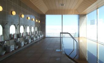 a modern bathroom with multiple toilets , sinks , and mirrors , as well as a large window overlooking the ocean at Route Inn Grantia Hakodate Ekimae