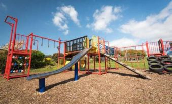 a colorful playground with swings , slides , and other play equipment , set against a backdrop of trees and a clear blue sky at The Chequers Inn