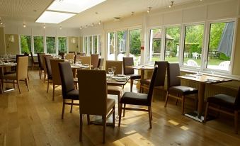 a large dining room with wooden floors , tables and chairs , and a view of trees outside the windows at Little Silver Country Hotel