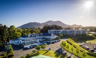 a large white building with a parking lot in front of it , surrounded by trees and mountains at Hilton Lake Taupo