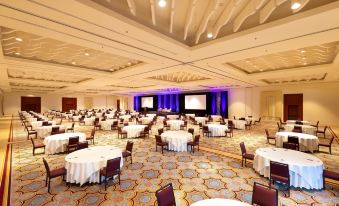 a large conference room with multiple round tables and chairs , a stage at the front , and blue lights illuminating the room at Sheraton Puerto Rico Resort & Casino