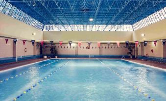 a large indoor swimming pool with a blue ceiling and walls , surrounded by benches and chairs at Hotel Mercure Gdynia Centrum