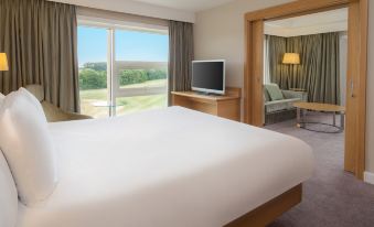 a hotel room with a large bed , a television , and a window overlooking a golf course at Hilton at St.George's Park, Burton Upon Trent