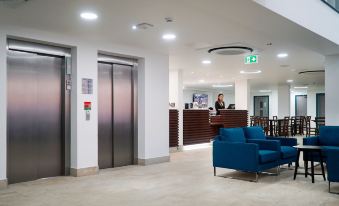 a modern office lobby with a blue couch , wooden reception desk , and an elevator in the background at Best Western Plus London Croydon Aparthotel