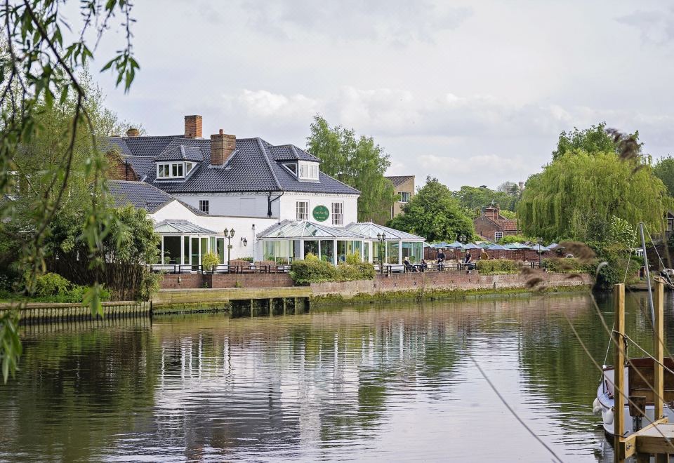 a large white building situated on the bank of a river , with several tents and umbrellas set up in front of it at Waveney House Hotel