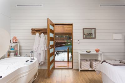 a bathroom with a bathtub and wooden doors that open onto a balcony , creating a view of the water at The Swan Valley Retreat