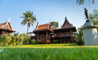 a large wooden house surrounded by a lush green lawn , with palm trees in the background at Maikaew Damnoen Resort
