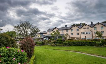 a large building with a red roof is surrounded by greenery and flowers , with a cloudy sky in the background at Arklow Bay Hotel