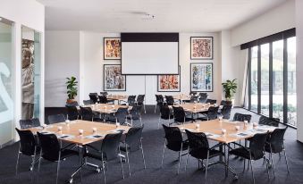 a conference room with multiple tables and chairs arranged for a meeting or event , with a projector screen on the wall at The Larwill Studio Melbourne - Art Series