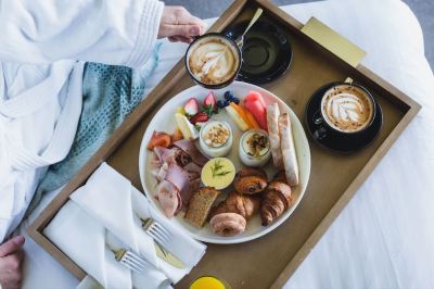 a woman is sitting at a dining table with a tray of breakfast items , including coffee and pastries at Oval Hotel at Adelaide Oval, an EVT hotel