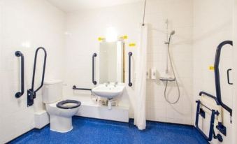 a bathroom with blue flooring and white walls , featuring a toilet , sink , shower head , and safety rails at Travelodge Ludlow Woofferton