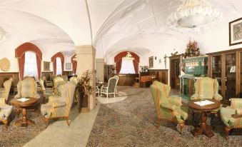 a large , ornate room with a high ceiling and white walls , featuring colorful chairs and a table at Hotel Dolomiti Schloss