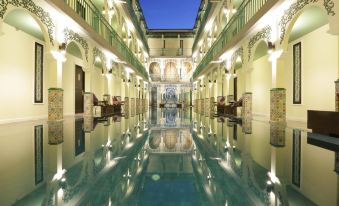 a long , narrow pool with a few chairs and tables in the middle is surrounded by white walls at Palette the Grand Morocc Hotel