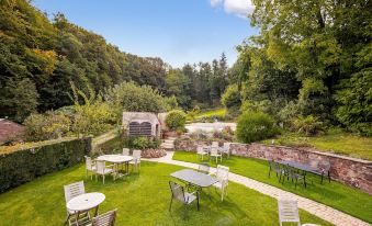 a lush green garden with tables and chairs arranged for a gathering , surrounded by trees and a stone archway at Castle of Comfort Hotel