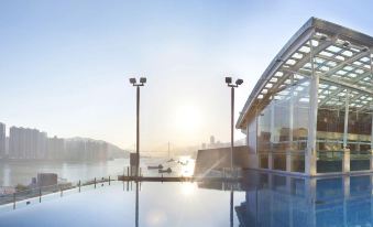 A large pool with buildings in the background is featured at an exotic swimming park at Nina Hotel Tsuen Wan West