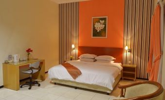 a modern hotel room with an orange wall , white bed , desk , and two bedside lamps at Hotel Kings Kudus