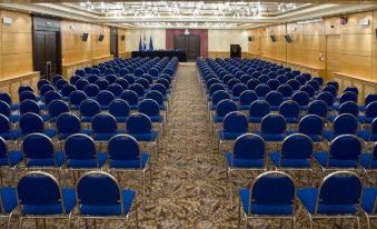 a large conference room with rows of blue chairs and a podium at the front at Corfu Palace Hotel