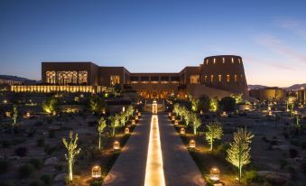 a large building with a long walkway in front of it , surrounded by trees and lit up with lights at Anantara Al Jabal Al Akhdar Resort