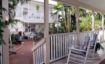 a porch with a white rocking chair , surrounded by potted plants and chairs , overlooking a courtyard filled with palm trees at Sabal Palm House Bed and Breakfast
