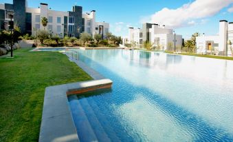 a large , empty swimming pool surrounded by lush green grass and modern buildings in the background at El Plantío Golf Resort