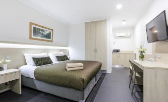 a modern hotel room with a large bed , white walls , and wooden furniture , including a desk and chairs at Morphettville Motor Inn