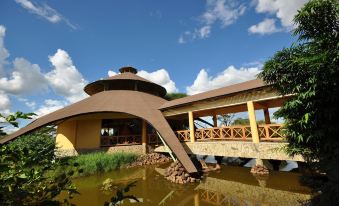 a modern building with a curved roof and wooden decking , situated near a pond and surrounded by trees at Kilima Safari Camp