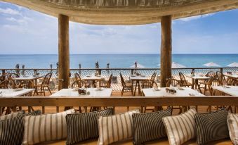 a restaurant with a dining area overlooking the ocean , featuring wooden tables and chairs arranged for guests to enjoy their meals at The Westin Resort, Costa Navarino