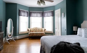 a cozy bedroom with hardwood floors , blue walls , and a large window that opens to a balcony at Sunset Hill House