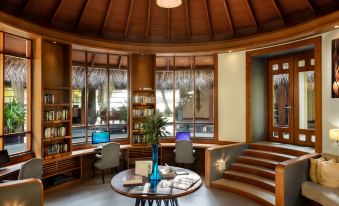a modern , well - lit room with wooden furniture and large windows offering views of the outdoors at Anantara Dhigu Maldives Resort - Special Offer on Transfer Rates for Summer 2024