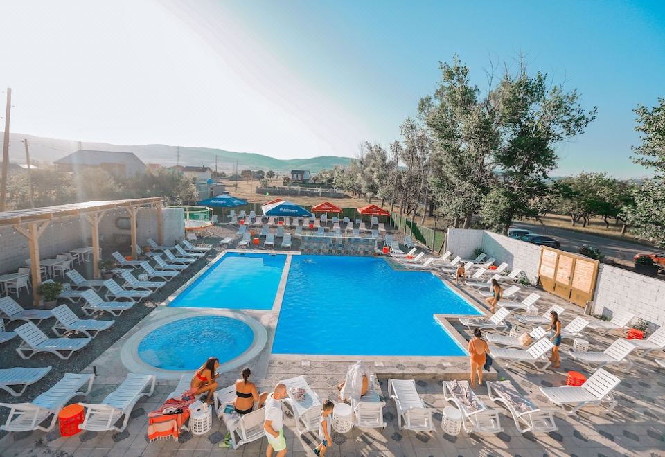 a large outdoor swimming pool surrounded by lounge chairs and umbrellas , with people enjoying their time in the water at Laguna Beach Club Bazaleti Lake
