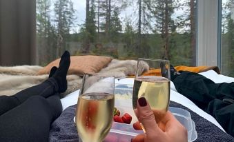 two people are sitting on a bed , holding wine glasses filled with a white drink at Arctic Skylight Lodge