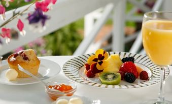 a plate of fruit , including strawberries , kiwi , and raspberry , sits on a dining table with a cup of coffee nearby at The Inn & Tavern at Meander