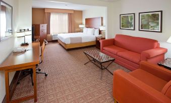 a hotel room with a bed , desk , and chairs , as well as an orange couch and coffee table at La Quinta Inn & Suites by Wyndham Bannockburn-Deerfield
