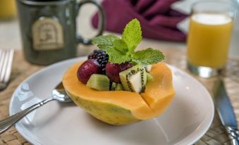 a bowl filled with a variety of fresh fruits , including apples , oranges , and bananas , placed on a dining table at The Old Wailuku Inn at Ulupono