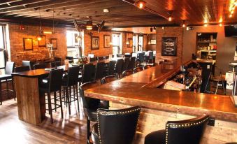 a well - lit restaurant with wooden tables and chairs , as well as a bar area with stools at Cornerstone Inn