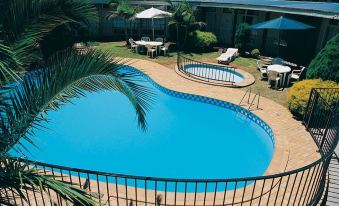 a large outdoor swimming pool surrounded by a patio area , with several lounge chairs and umbrellas placed around it at Jacksons Motor Inn