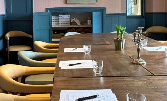 a long wooden table is set with papers , glasses , and a pen , in a room with blue walls at The Barnsdale, Rutland