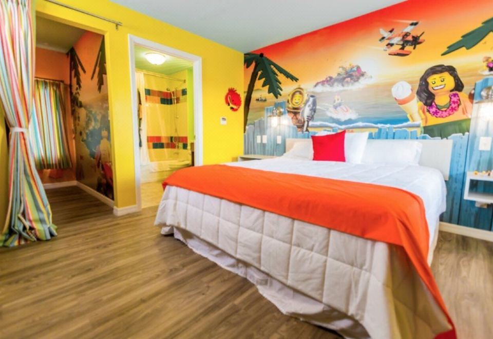 a large bed with orange and white bedding is in a room with yellow walls at Legoland Beach Retreat