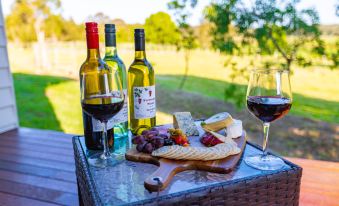 a table with two wine bottles , cheese , and crackers is set up outdoors in a grassy area at Narangba Motel (Formerly Brisbane North B&B and Winery)