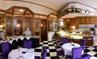 a dining room with a black and white checkered floor , purple chairs , and a buffet table filled with food at Hotel Alexandra