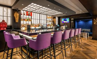 a modern bar with a purple bar stools and a television mounted on the wall at The Kingsley Bloomfield Hills - a DoubleTree by Hilton