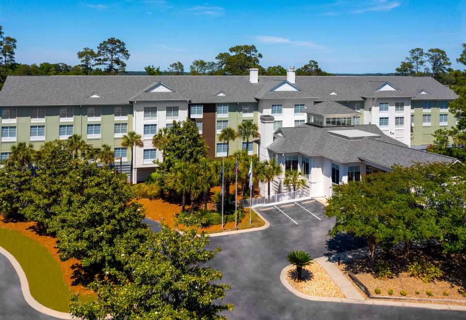 an aerial view of a building surrounded by trees and grass , with a parking lot in the foreground at Hilton Garden Inn Hilton Head