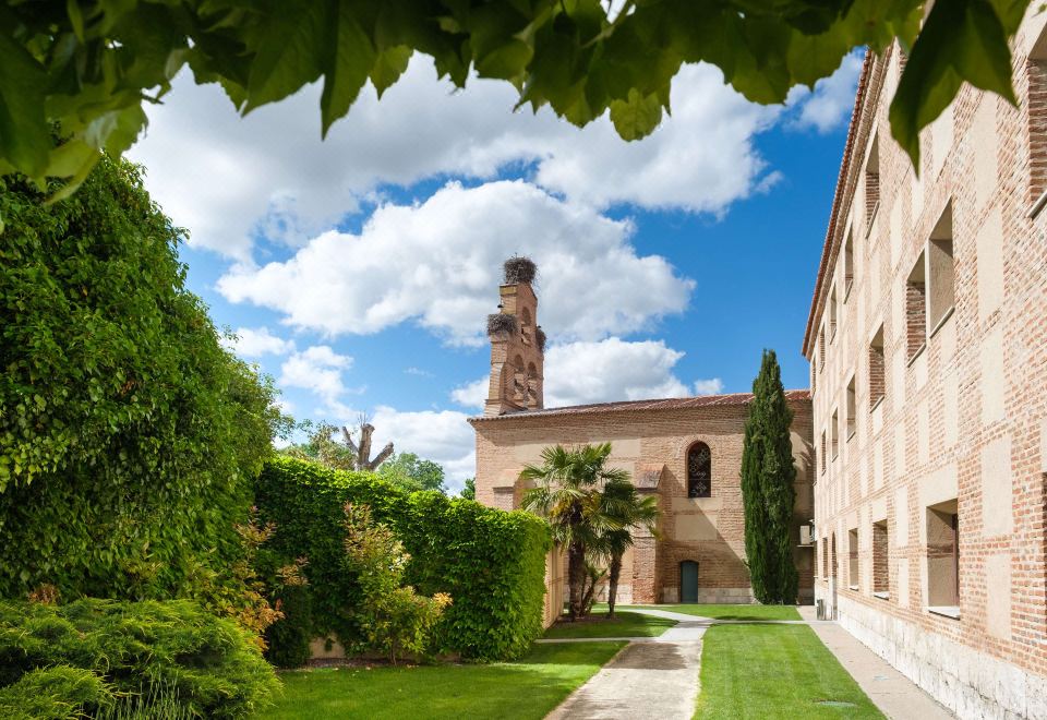 a view of a garden with a tall tower in the background , surrounded by green plants at Castilla Termal Olmedo
