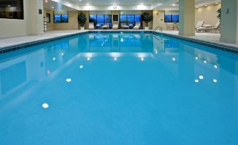 a large indoor swimming pool with blue water , surrounded by white walls and multiple windows , under a sunny sky at Holiday Inn Wilmington