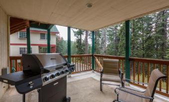 a wooden deck with a grill and chairs overlooking a green building , under an open ceiling at Inside Yosemite Lower Cascades