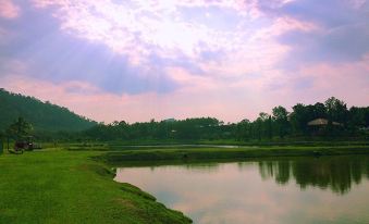 a serene landscape with a body of water surrounded by green grass and trees , under a cloudy sky at Kampung Bongsu Farmstay